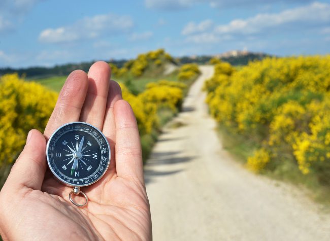 Compass in the hand against rural road Compass in the hand against rural road